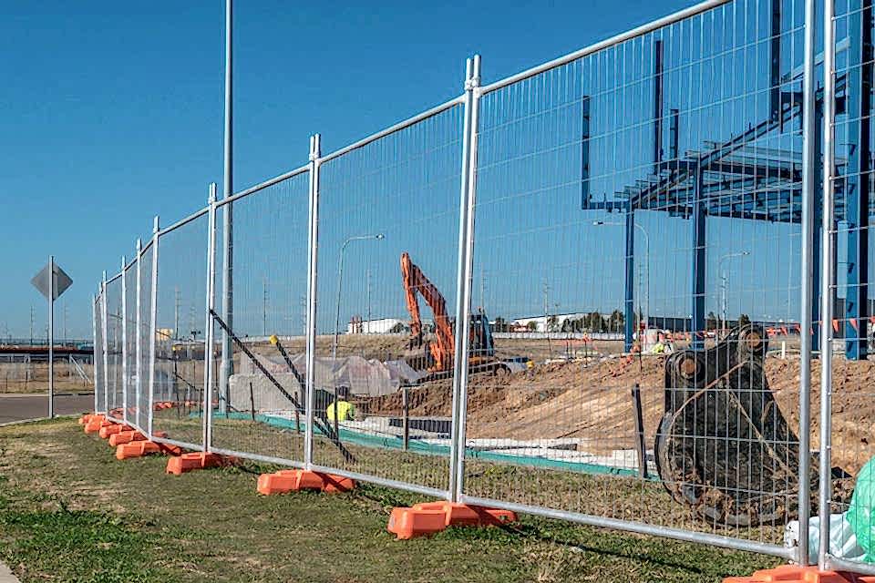 A digger is working in the construction site enclosed by Australia temporary fence.