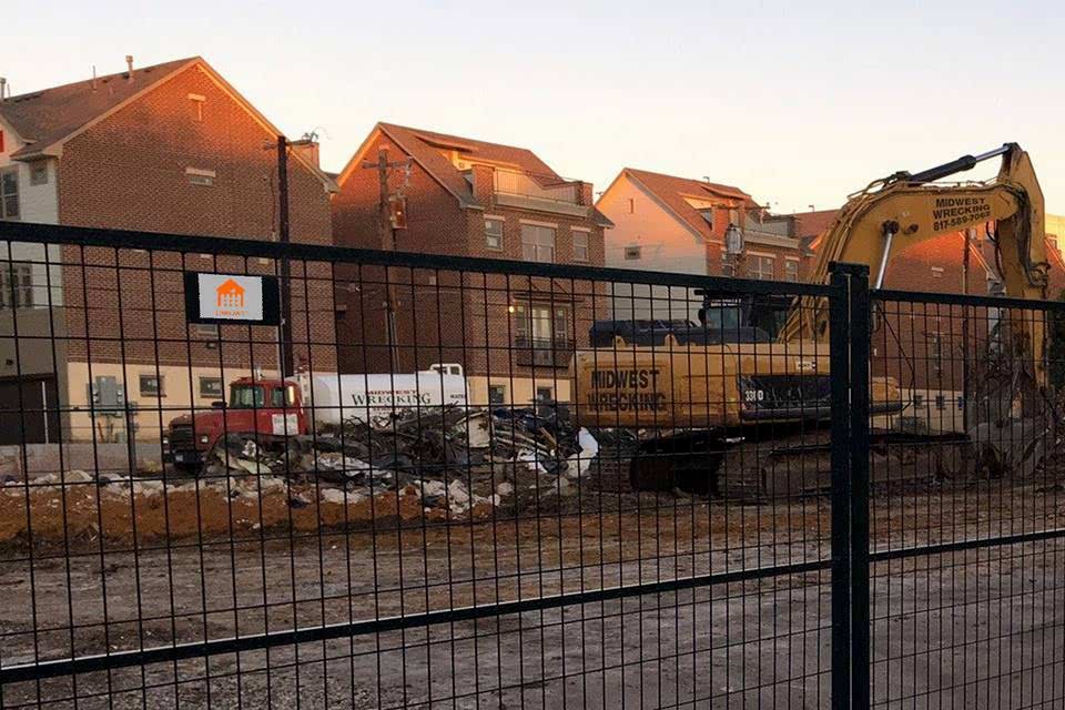 A digger is digging the working in the construction site next to a residential community that is enclosed by a black Canada temporary fence.