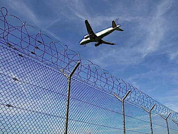 An airplane is flying over the chain link fence equipped with razor wires.