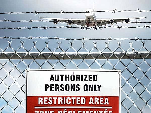 An airplane is flying over the chain link fence equipped with barbed wires.