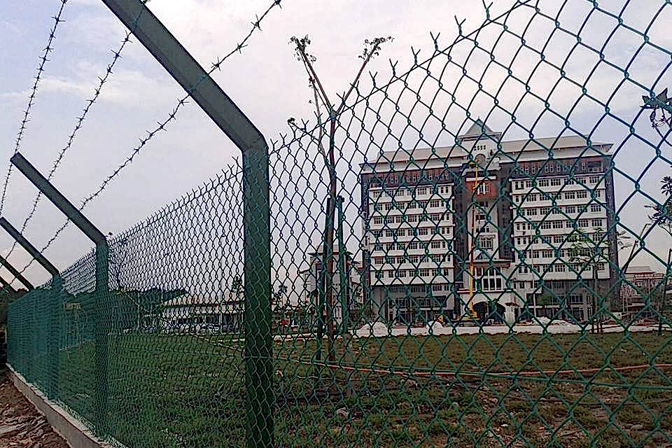 Chain link fence with barbed wire topping is placed along the industrial building.