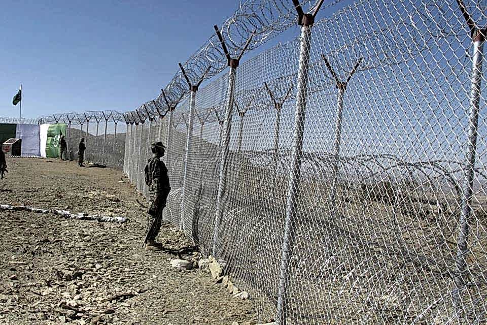 Soldiers are standing along the chain link fence with a concertina topping.