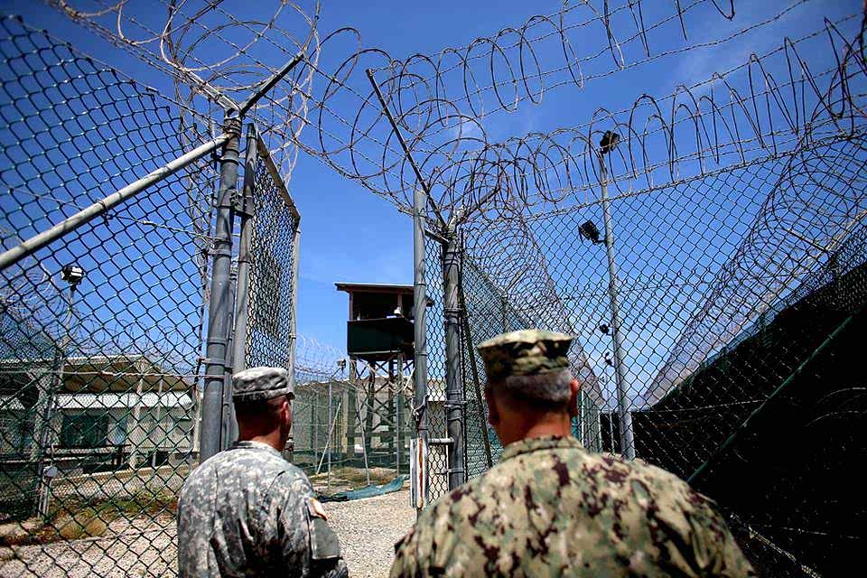 Tow soldiers are checking the watch tower encircled by chain link fence with a concertina topping.