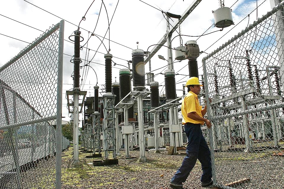 A maintenance worker opens the chain link fence gate for power facility inspection.