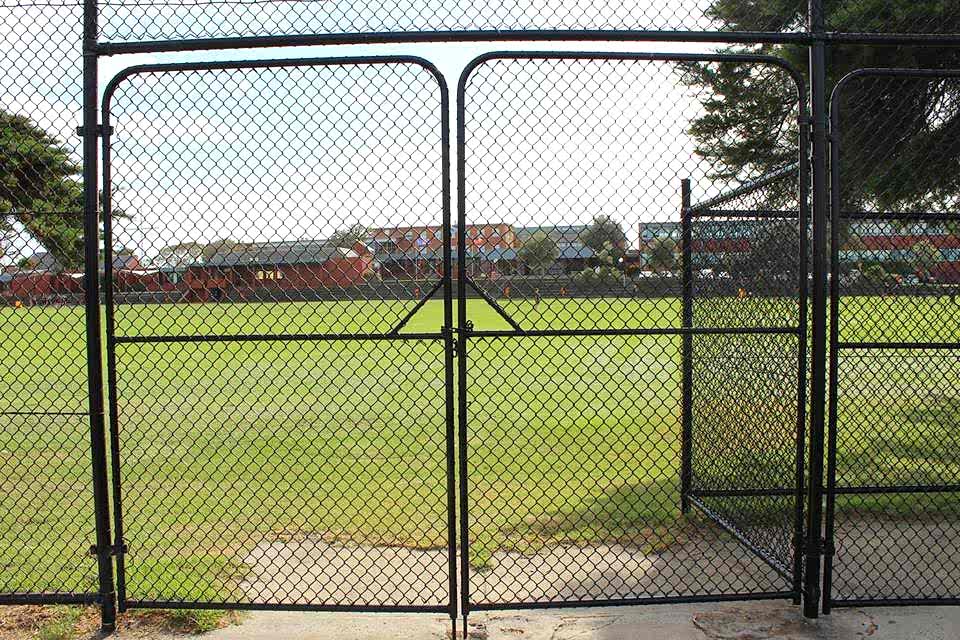 Sports field gate made of chain link fence is closed.