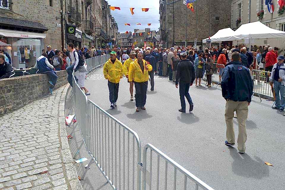 Many people are walking on the street that placed crowd control barrier on both sides of the street.