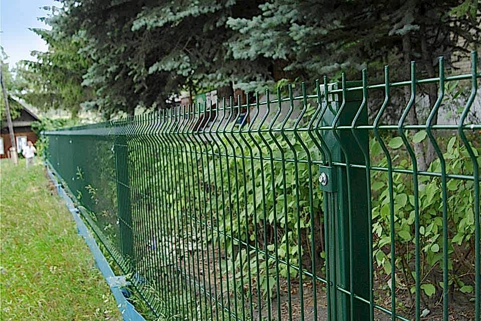 Many trees and plants are planted in a park enclosed by curvy welded fence.