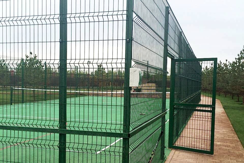 A sports field is enclosed by curvy welded fence.