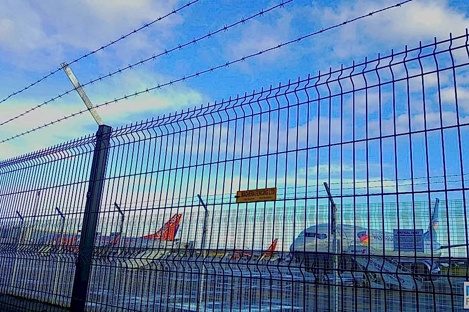 Green curvy welded mesh fences with barbed wires are installed in the airport