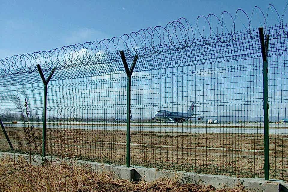 Green curvy welded mesh fences with razor wires are installed in the airport.